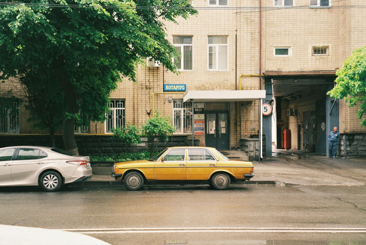 Yellow vintage car parked outside a brick building beneath green trees