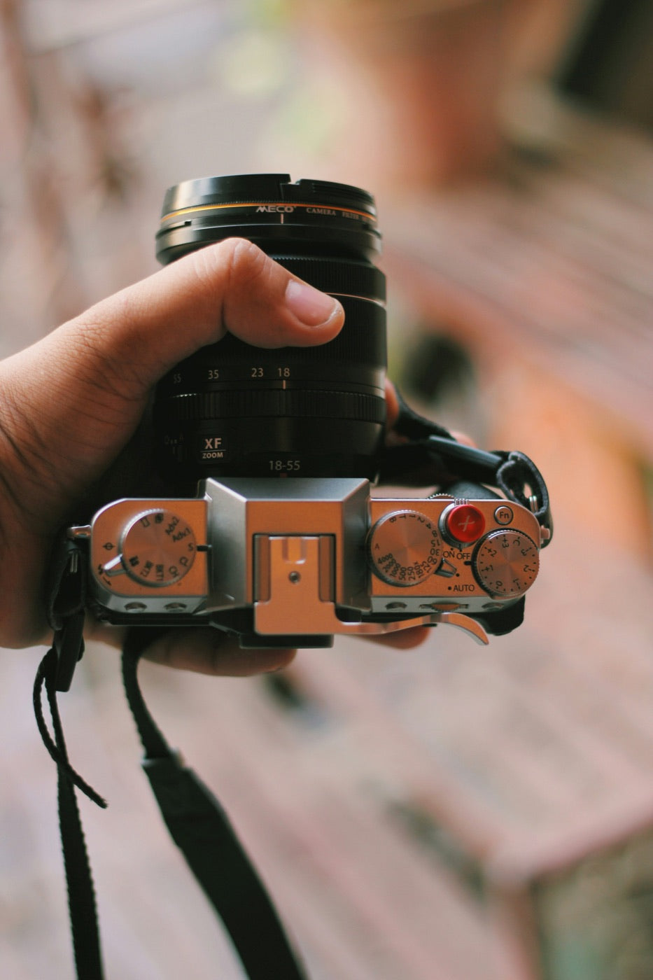 Hand holding a silver camera with the ISO dial visible on its top plate