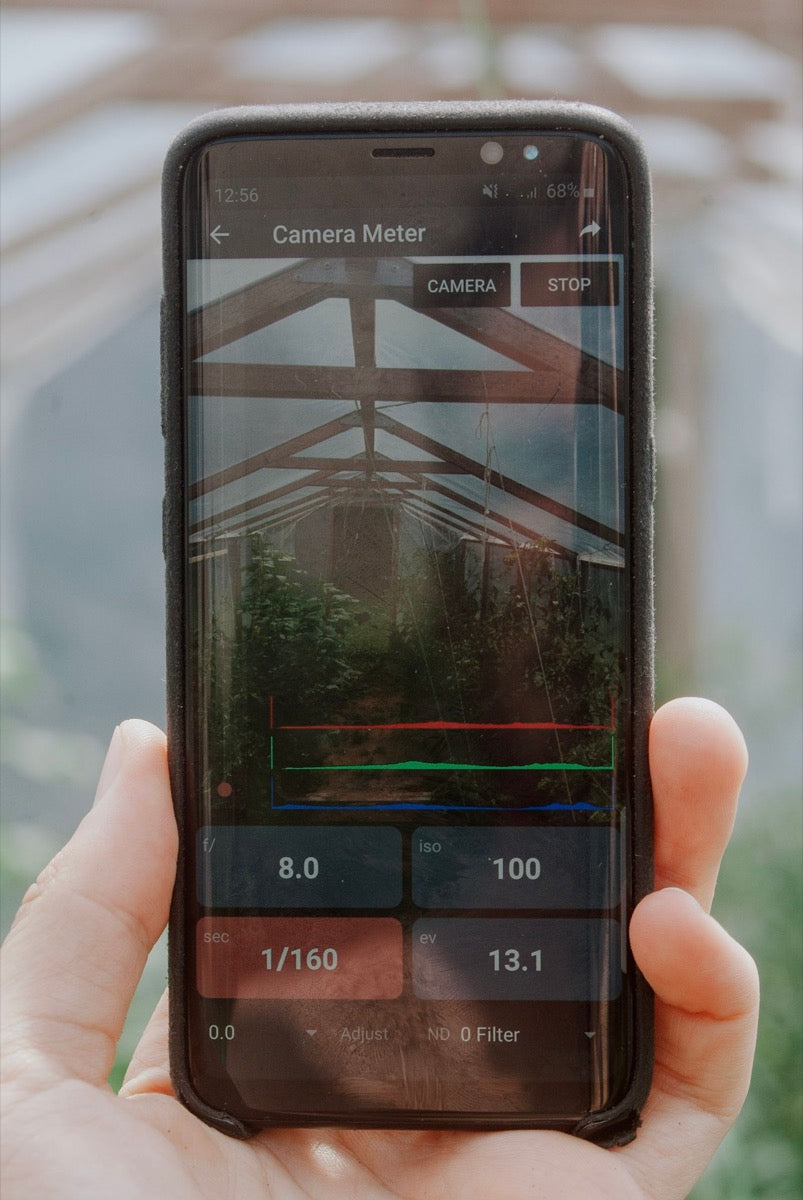 Hand holding a smartphone displaying a camera light-meter application