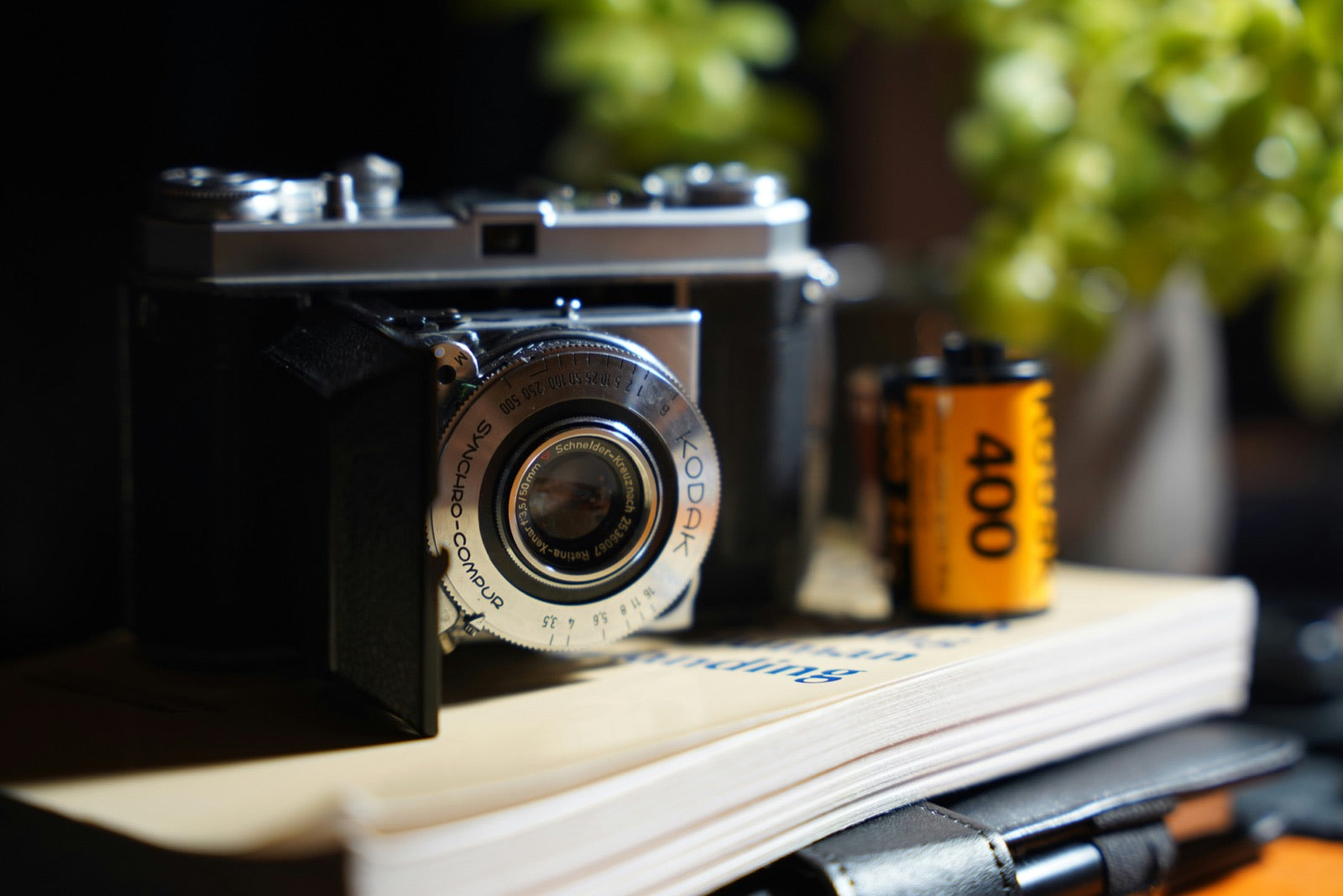 Vintage Kodak film camera beside a roll of Kodak 400 film on stacked books outdoors