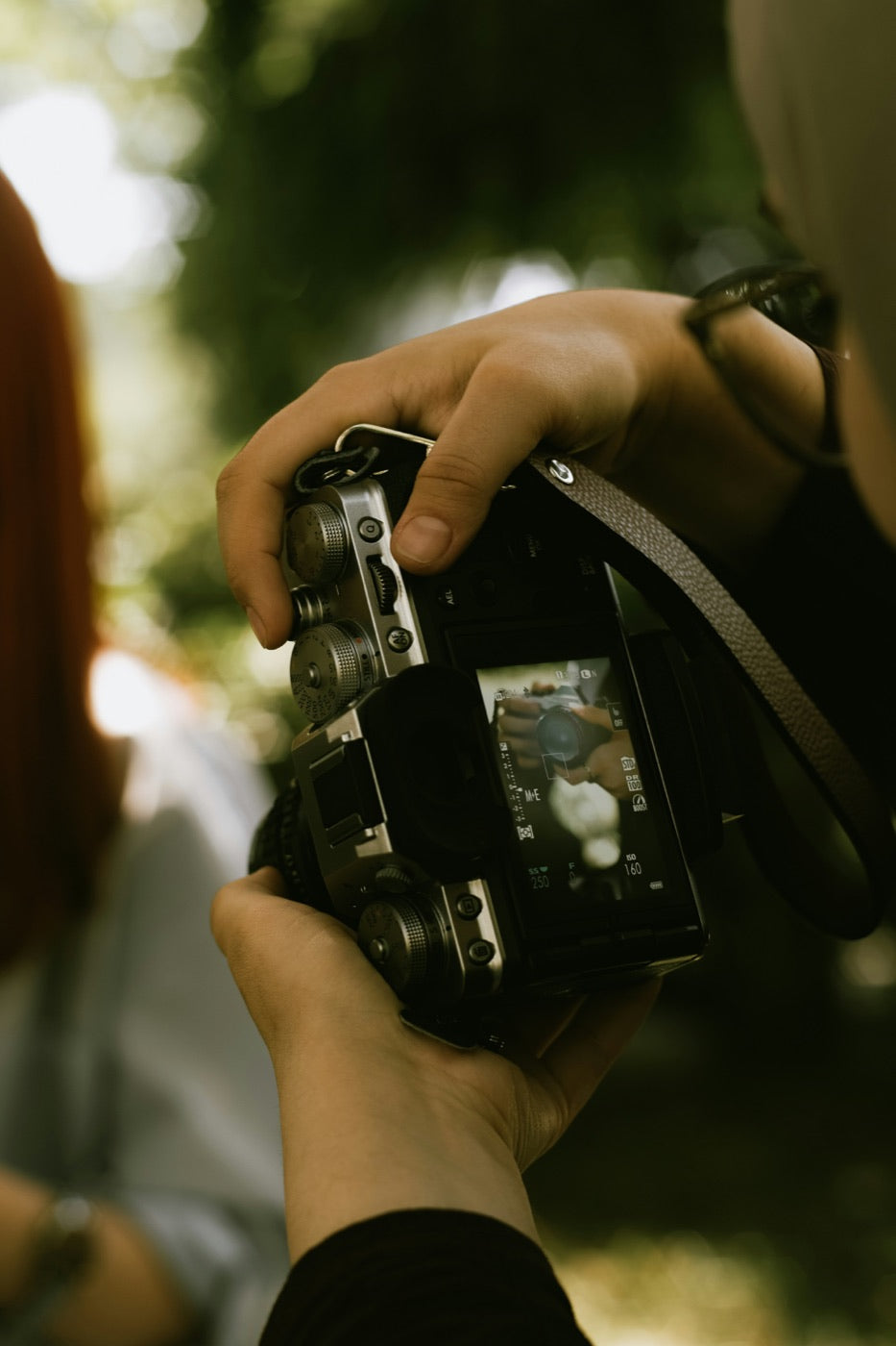 Hands holding a digital camera outdoors with a portrait framed on the rear screen