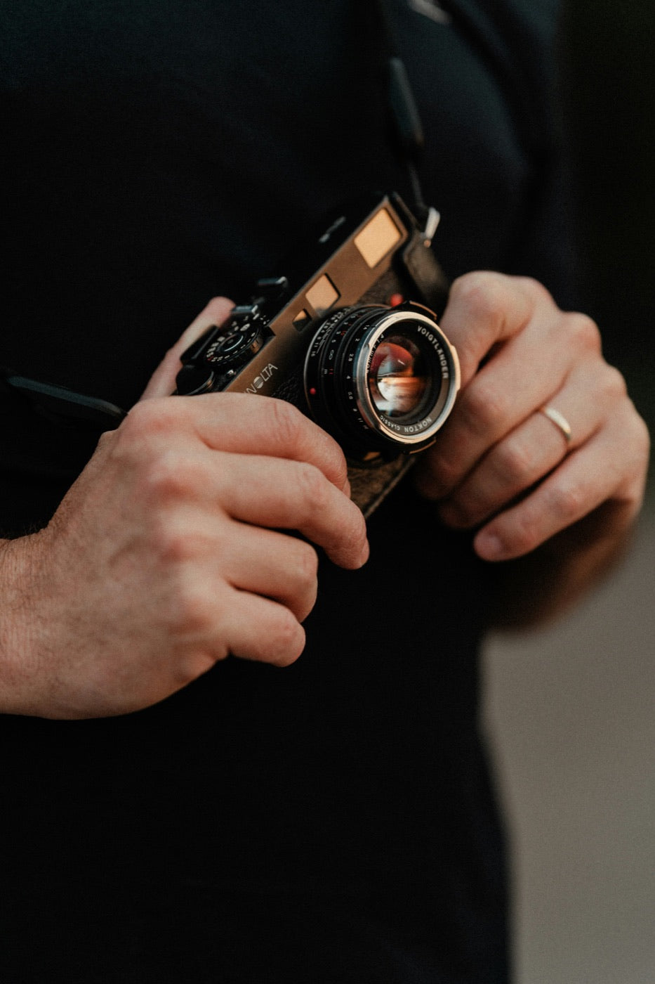 Hands holding a compact Voigtlander film camera against dark clothing