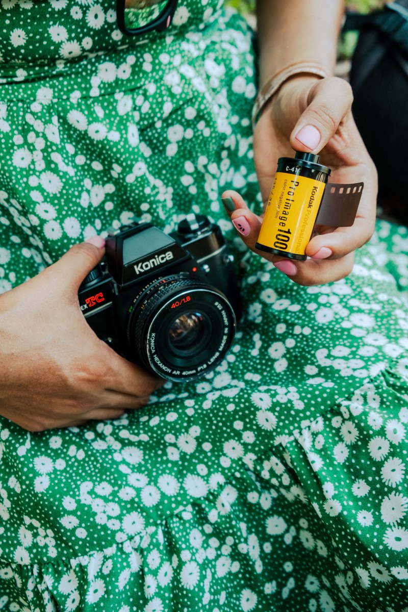 Person holding a Konica film camera and a roll of Kodak Pro Image 100 film